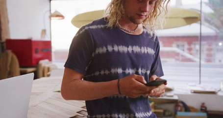 Caucasian male surfboard maker standing in his studio and using his smartphone - Powered by Adobe