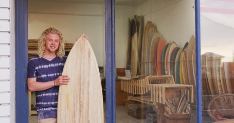 Caucasian male surfboard maker holding a brand new surfboard  - Powered by Adobe