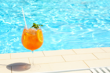 Glass of delicious cocktail near swimming pool, space for text. Refreshing drink