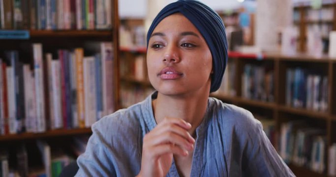 Asian female student wearing a blue hijab thinking and learning her chin on her hand