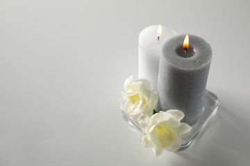 Fototapeta na wymiar Wax candles and flowers in glass holder on white table. Space for text