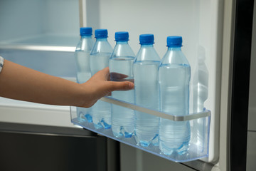 Woman taking bottle of fresh water from fridge door bin, closeup