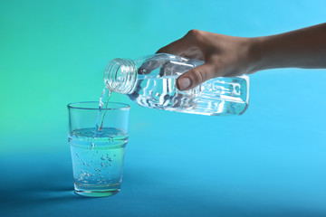 Woman pouring water from bottle into glass on blue background, closeup