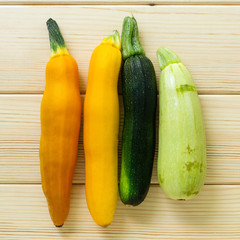 Green and yellow young zucchini on a light wooden background