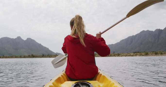 Caucasian woman having a good time on a trip to the mountains, kayaking on a lake, holding a paddle