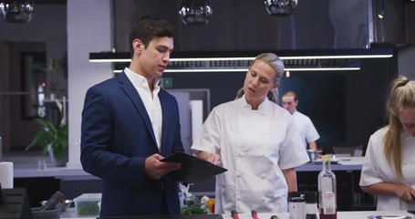 Caucasian male restaurant manager in the kitchen talking to a Caucasian female cook, giving instruct