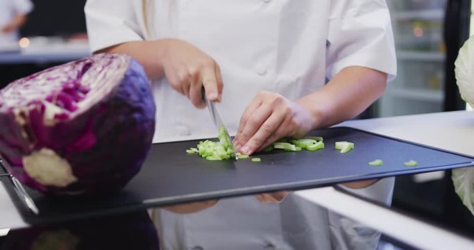 Caucasian female cook working in a restaurant kitchen,slicing celery on a cutting board