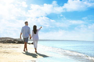 Young couple walking on beach near sea, back view. Honeymoon trip