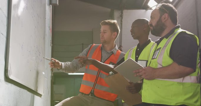 Two Caucasian and an African American male factory worker at a factory in discussion 