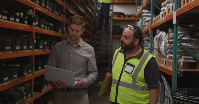 Two Caucasian male factory workers at a factory making hydraulic equipment in discussion