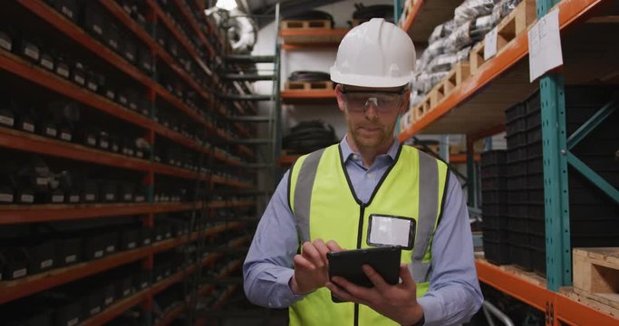 Caucasian male factory worker at a factory wearing a high vis vest using a tablet computer