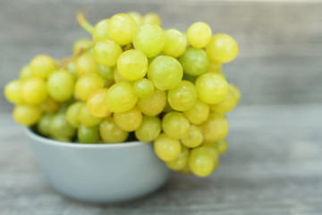 A bunch of ripe green grapes in a gray container on a gray background.