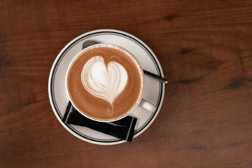 Close up coffee cup with latte art milk foam on wood table, top view