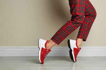 Woman wearing stylish sneakers near beige wall indoors, closeup
