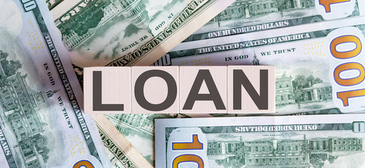Concept words LOAN on wooden blocks on a beautiful background from dollar bills.