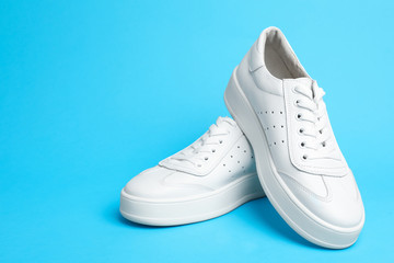 Stylish white shoes on light blue background. Space for text