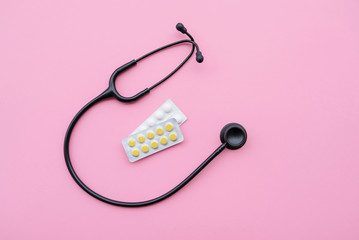 Black modern stethoscope and tablets on pink background.