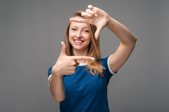 Portrait of positive young blonde female with cheerful expression, gestures finger frame actively at camera