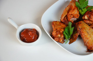 plate of chicken wings on white table red sauce in a gravy boat