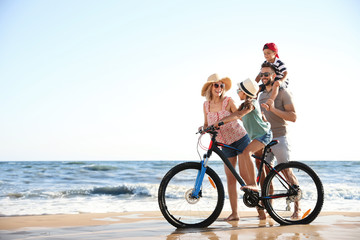 Fototapeta premium Happy family with bicycle on sandy beach near sea