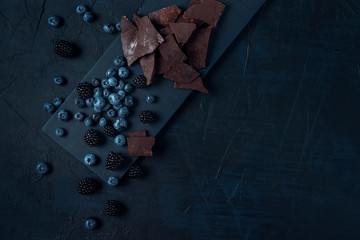 Blueberry and blackberry with chocolate pieces on the black cutting board and dark textured background. Flat lay. Copy space.