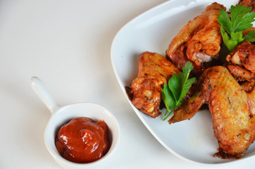 plate of chicken wings on white table red sauce in a gravy boat