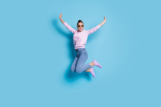 Full length photo of cheerful candid energetic girl jump enjoy weekend raise hands wear good look pullover isolated over blue color background