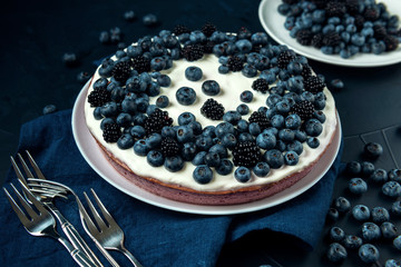 Cottage cheese casserole and plate with blackberry and blueberry on dark textured background. Sweet pie with cutlery on the table.