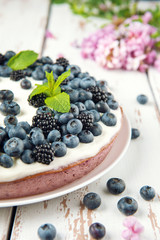 Cottage cheese casserole with blackberry and blueberry on white Provence style table. Sweet pie with acacia flowers on white backdrop.