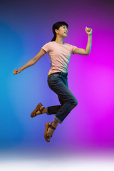 Fototapeta na wymiar Happy. Jumping high asian young woman's portrait on gradient studio background in neon. Beautiful female model in casual style. Concept of human emotions, facial expression, youth, sales, ad.