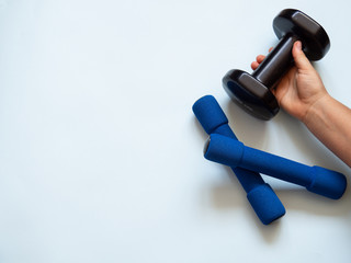 Two blue small dumbbells and a caucasian woman hand grabbing one black dumbbell for weight and strength training in white background. Copy space for text. Weightlifting and healthy lifestyle concept