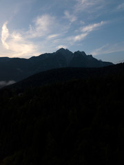 Aerial view of Dolomites Alpine mountains, forest in shadow against sun, blue sky with clouds. Nature landscape Tyrol, North of Italy, Europe