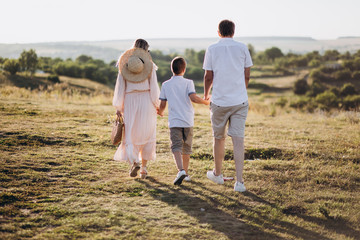 Happy family: mom, dad and child son are walking in the meadow in summer, nature background. back view