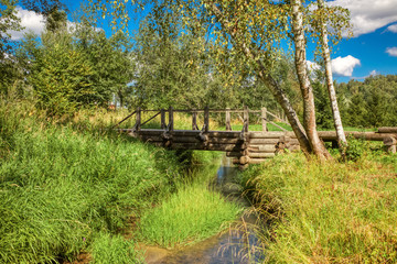 Fototapeta na wymiar A wooden bridge over a forest stream against the blue sky on a Sunny summer day.