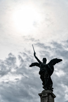 Statue of an angel in Rome with sword and clouds background with sun rays as divine light