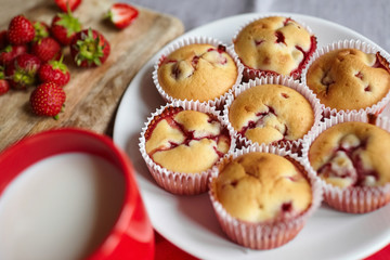 Strawberry muffins on white plate with cup of milk and fresh berries