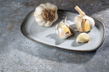 Garlic on a plate and a grey stone background, the healthy cloves lower blood pressure and inhibit...