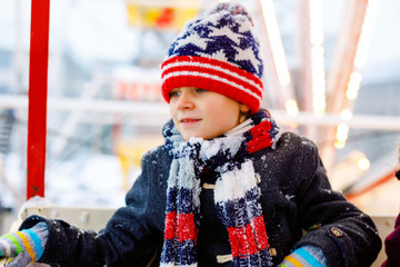 Little lovely kid boy having fun on ferris wheel on traditional German Christmas market during strong snowfall. Happy healthy child enjoying family market in Germany. Lovely schoolboy.