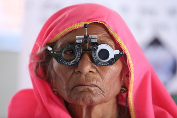 Old Indian woman in pink mantilla from Rajasthan getting eyes tested. Eye camp. Eye patient. Weak eyesight. Eye Health. Eye examination by doctor. Healthcare to elderly. 