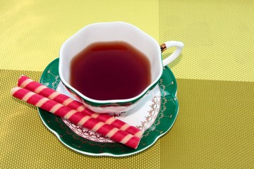 A Cup of tea with sweet tubes on a bright green background.