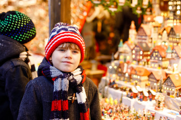 Two little kid boys selecting decoration on Christmas market. Beautiful siblings and best friends shopping for toys and decorative houses. Xmas market in Germany.