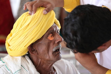 Old Indian man in Yellow turban from Rajasthan getting eyes tested. Eye camp. Eye patient. Weak eyesight. Eye Health. Eye examination by doctor. Healthcare to elderly. 