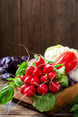 Assortment of vegetables in a wooden box on the table. A lot of different raw vegetables in the basket. Radish, garlic, sweet pepper and eggplant on the table. The concept of healthy eating. Close up