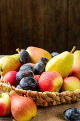 Assortment of fruits in a basket on the table. There are a lot of different raw fruits in the basket. Plums, peaches, apples and pears on the table. Healthy food concept	