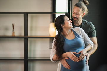 Fototapeta premium Handsome beard man take care his pregnant wife. Happy family in house concept.