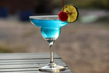 Juice that may contain alcohol to add flavor in a clear, round glass with a thin slice of kaffir lime garnish with a cherry.