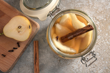 Glass jar with canned pears flavored with cinnamon and cloves on a rustic vintage stone background, high angle view from above, selected focus, narrow depth of field