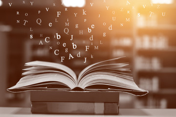 Open book on the table and English alphabet Floating above the book in the library and blur bookshelf background.