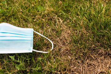 Used medical protective mask thrown on the grass.