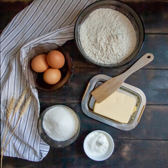 Baking ingredients for shortcrust pastry: butter, flour, eggs, sour cream, a towel on a wooden background. Flatley top view